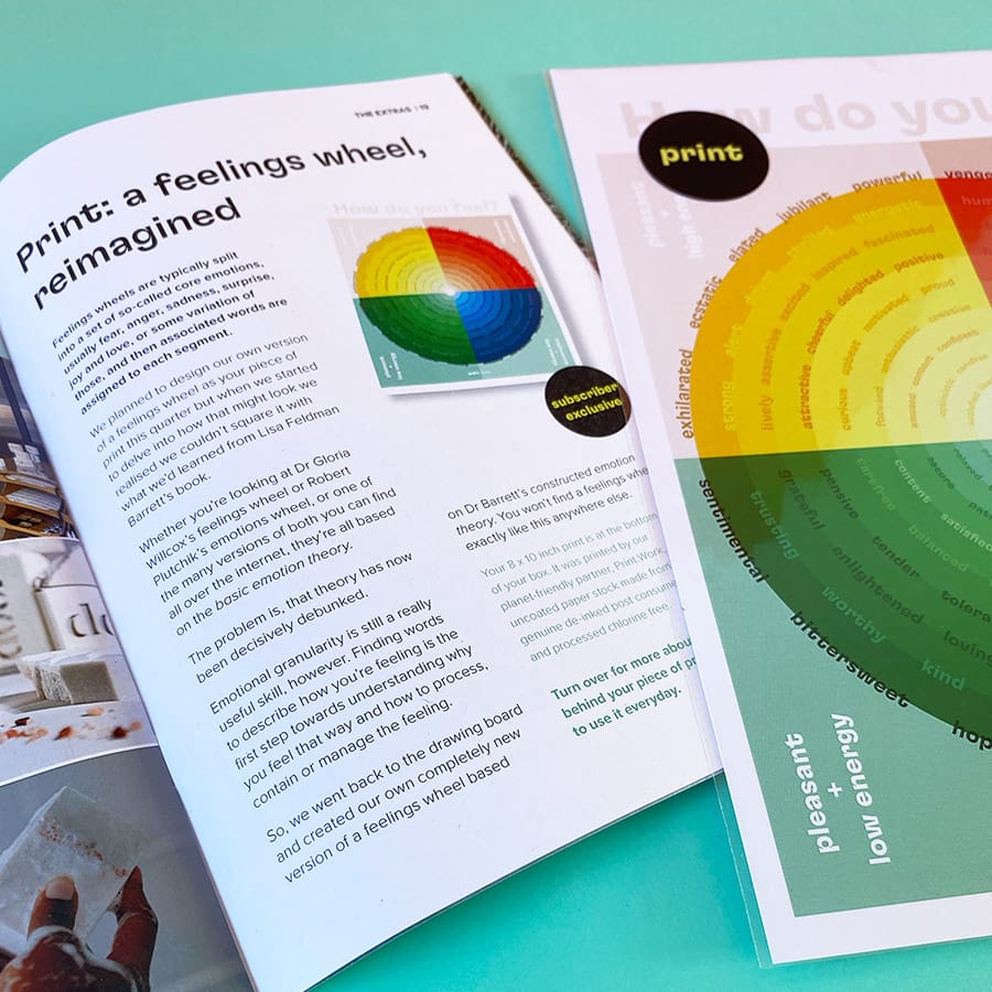 Magazine open at a page about a feelings wheel beside a printed version of the wheel in a clear compostable sleeve