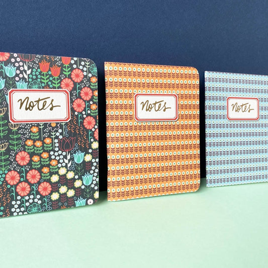 Three pocket sized notebooks with different floral covers and the word notes in gold foil