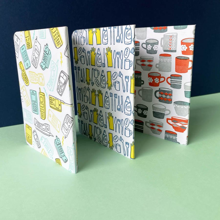 Three pocket sized letterpress notebooks with illustrated front and back covers